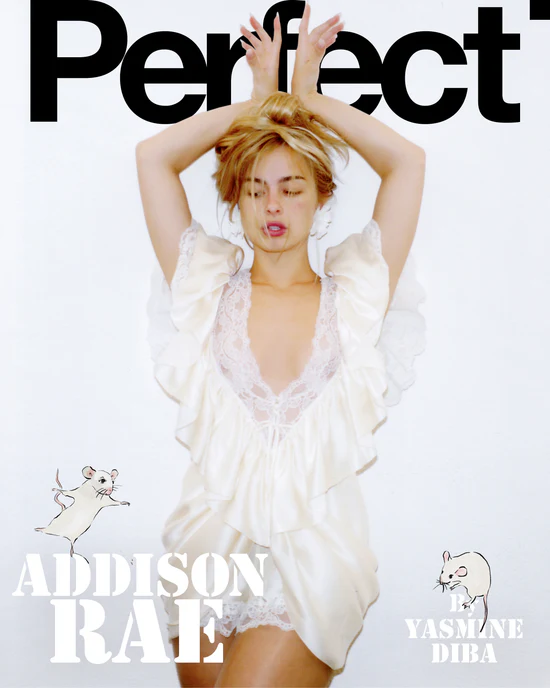 Addison Rae posing with arms raised in an ivory ruffled satin and lace dress against a white studio background.