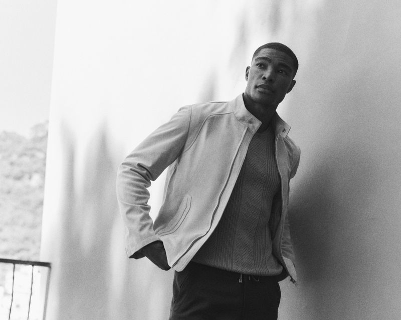 Model Niyo Malik wearing a light zip jacket and ribbed knit sweater in a black and white portrait for Brett Johnson.
