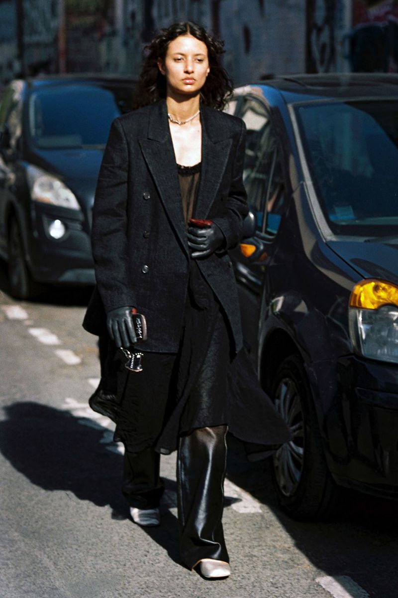 Model Alicia Lindén Guinez walking down a city street wearing an oversized black blazer, wide trousers, and leather gloves.