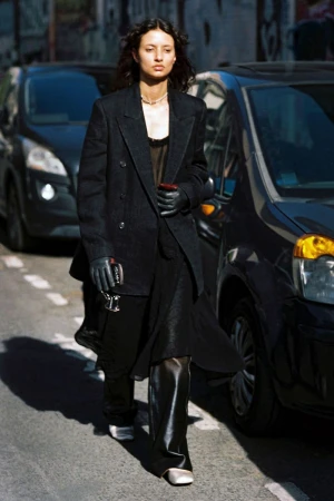 Model Alicia Lindén Guinez walking down a city street wearing an oversized black blazer, wide trousers, and leather gloves.