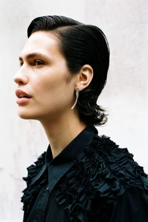 Model Alicia Lindén Guinez in profile wearing a black ruffled shirt and a sculptural silver earring.
