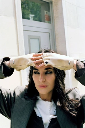 Alicia Lindén Guinez wearing fingerless cream gloves and a grey pinstriped blazer posed outdoors against a building entrance.