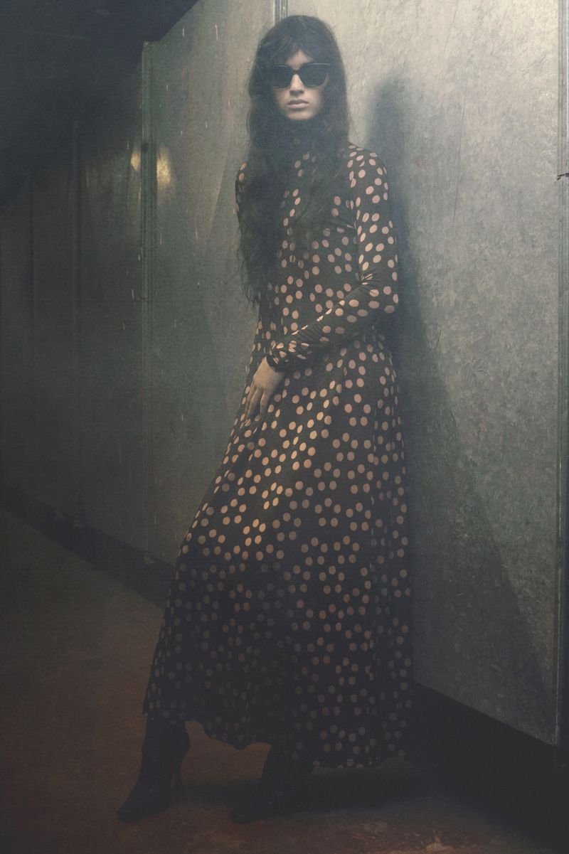 Model Svetlana Lethelier wearing a polka dot maxi dress and sunglasses leaning against an industrial metal wall.