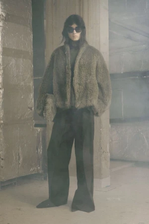 Model Svetlana Lethelier wearing an oversized textured jacket, sunglasses, and wide-leg trousers in a hazy industrial space.