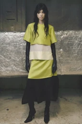 Model Svetlana Lethelier posing in a chartreuse layered top, skirt, and long black leather gloves against a foil-backed wall.