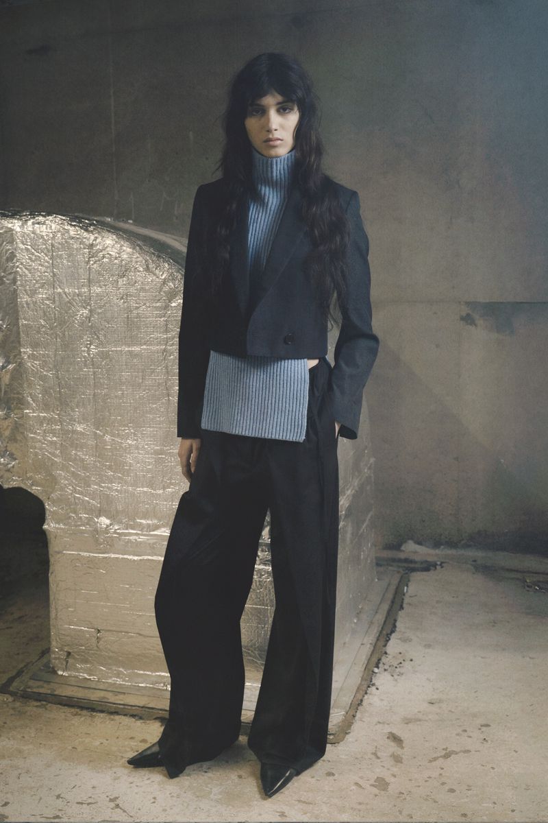Model Svetlana Lethelier wearing a cropped black blazer, light blue ribbed turtleneck, and wide-leg black trousers.