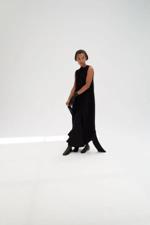Model wearing a black sleeveless dress and leather gloves standing on a white seamless background