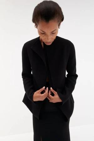 High angle shot of model Romae Gordon in a structured black jacket and skirt against a bright white background.