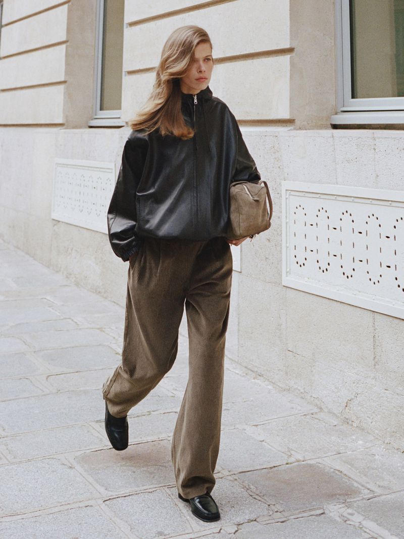 Model Bianca Huisman walking along a street wearing an oversized black leather jacket and wide-leg corduroy trousers.