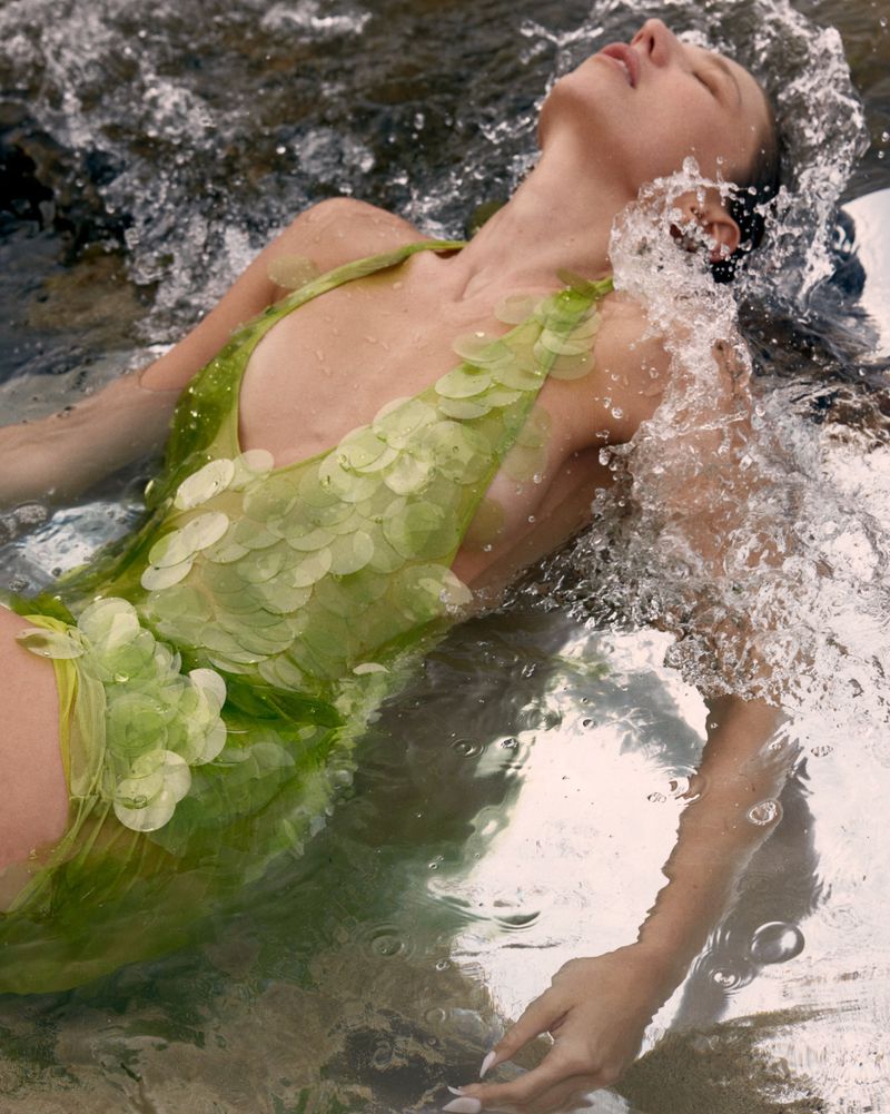 Woman in a lime green sequined dress floating in shallow ocean water with splashing waves.
