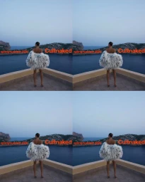 Model seen from behind wearing a voluminous white feather jacket overlooking the ocean from a terrace for Cult Naked.