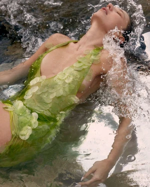 Woman in a lime green sequined dress floating in shallow ocean water with splashing waves.