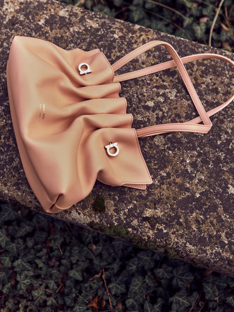 Peach-colored Salvatore Ferragamo handbag sits on a mossy stone wall, surrounded by lush green ivy in an outdoor setting.