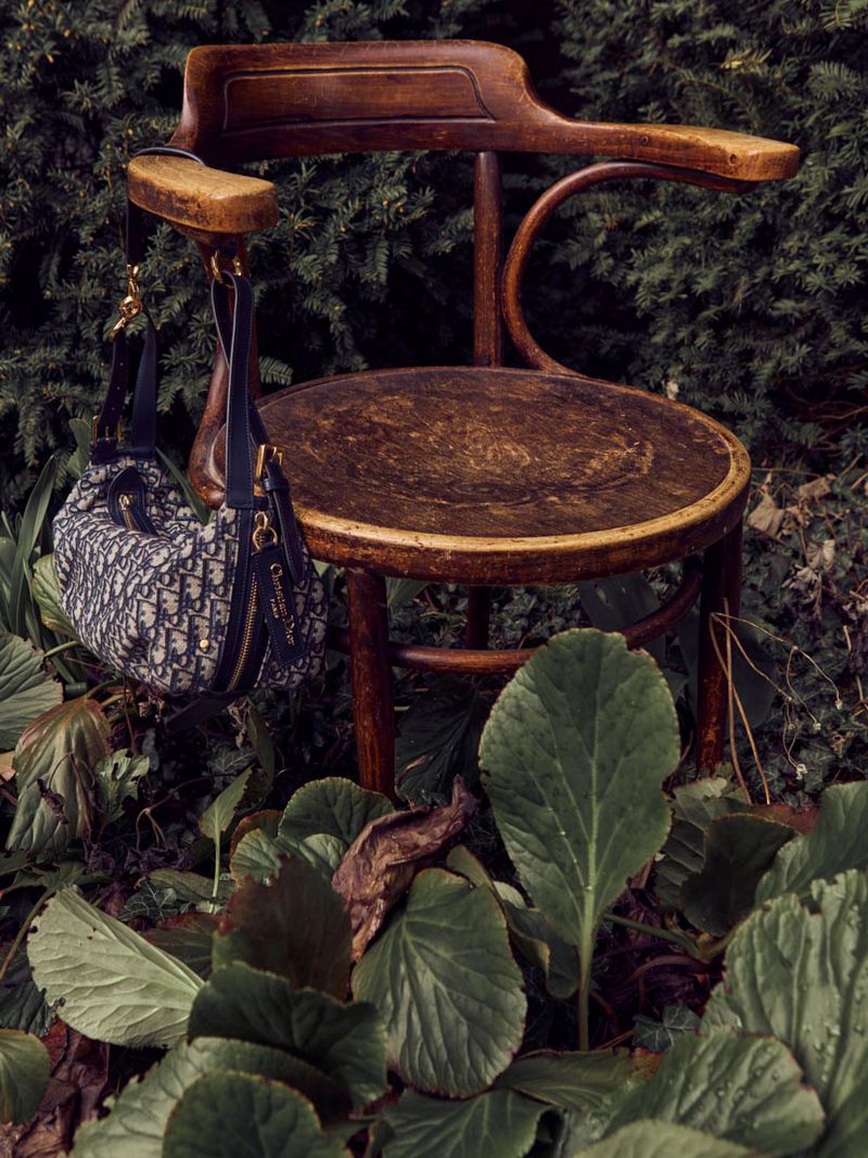 Brown wooden chair stands outdoors, lush greenery surrounds it, and a purse is hanging from the chair's arm. 