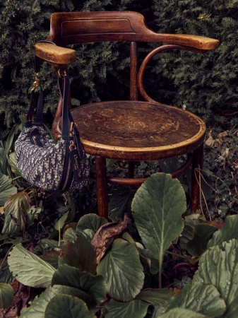 Brown wooden chair stands outdoors, lush greenery surrounds it, and a purse is hanging from the chair's arm. 