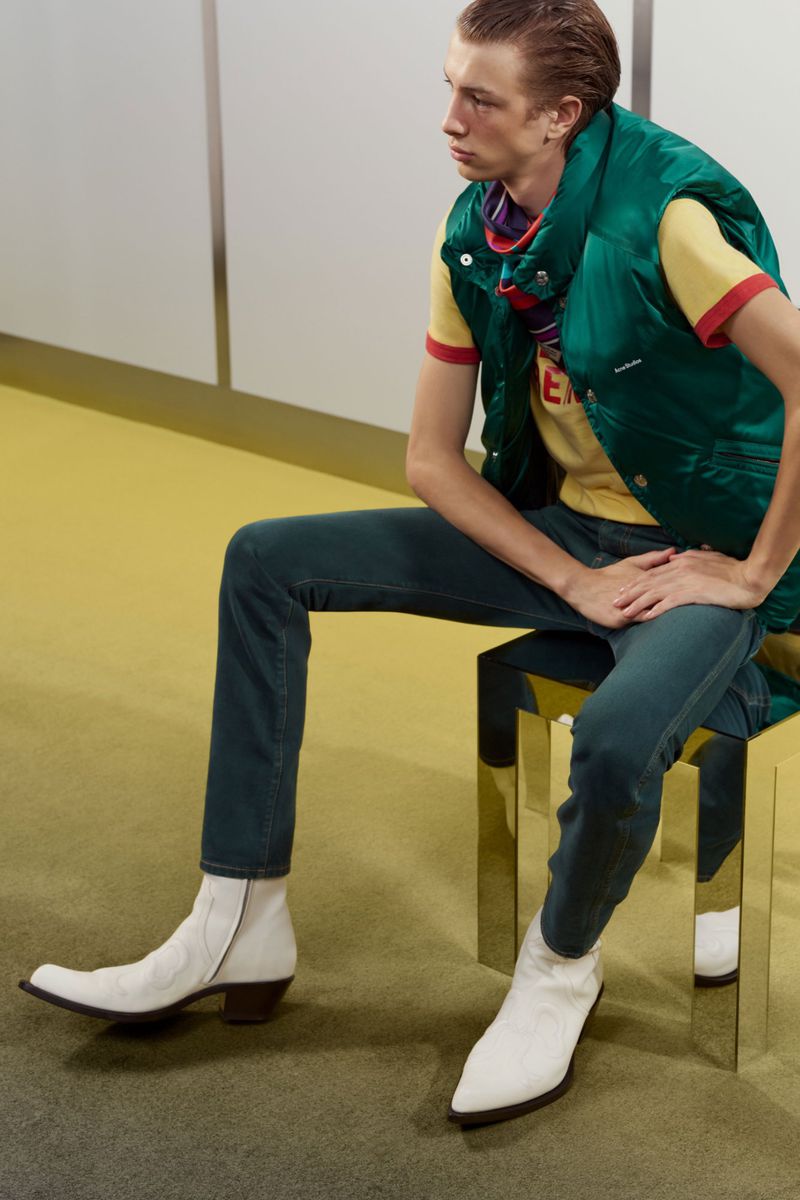 Pavlo Stinyk seated wearing an emerald green puffer vest, dark green trousers, and pointed white leather boots.