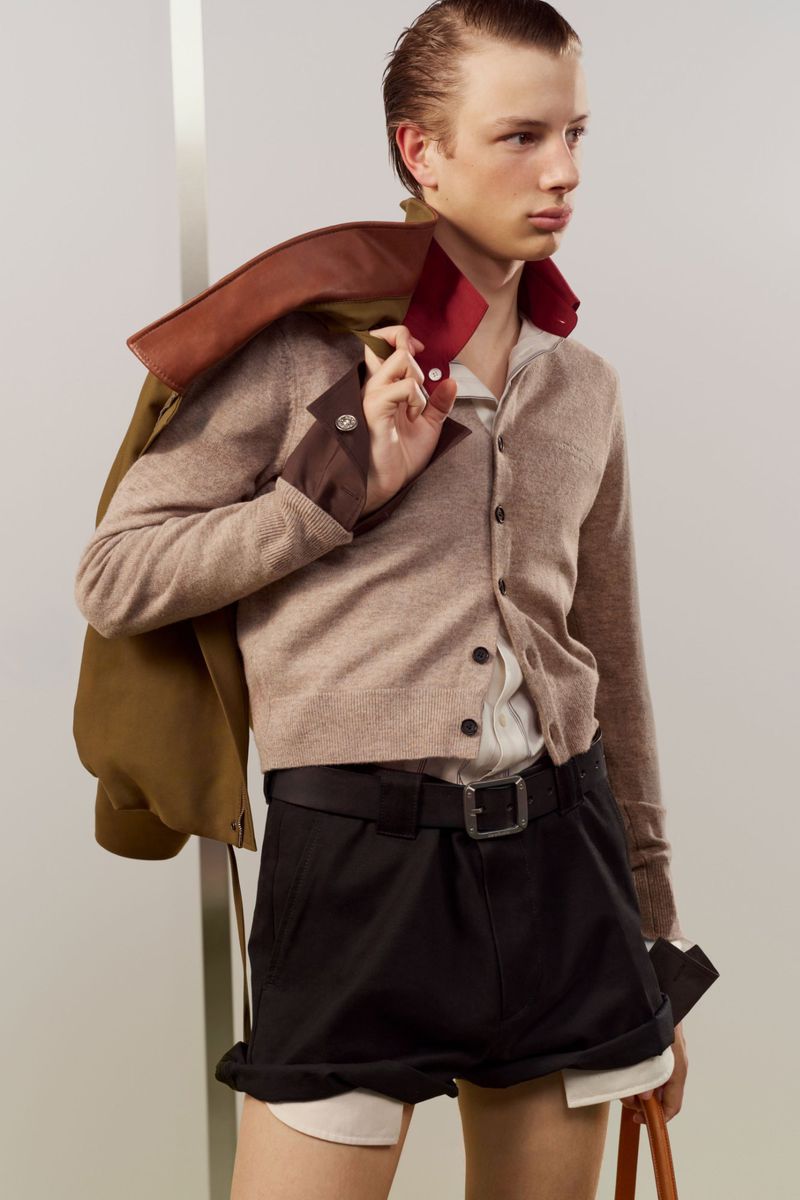 Model Pavlo Stinyk wearing a beige knit cardigan, layered shirt, and black cuffed shorts against a neutral studio backdrop.