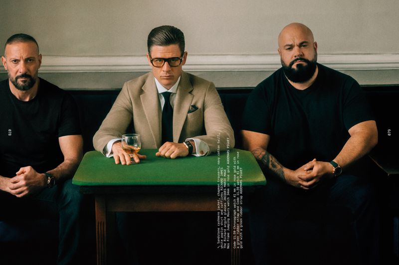 James Norton wearing a tan suit and glasses seated at a green table between two men in black shirts for Les Hommes Publics.