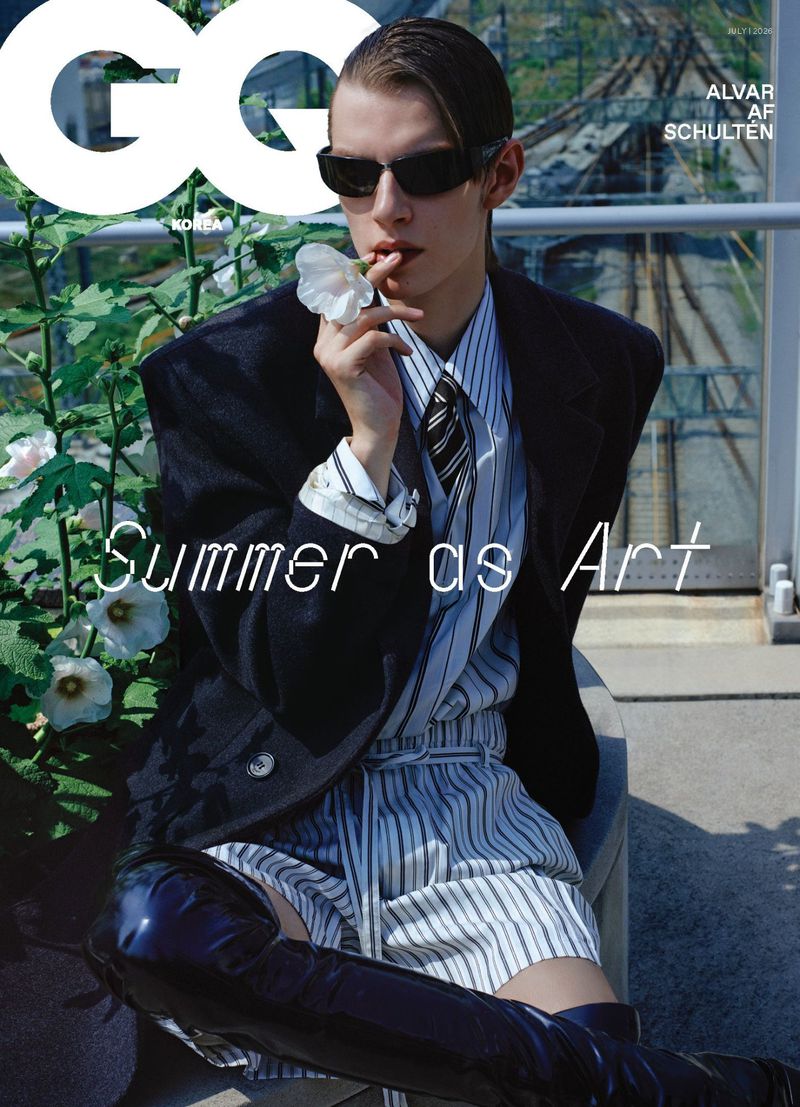 Model Alvar af Schulten seated in sunglasses, an oversized dark blazer, striped shorts, and black patent boots holding a white flower.