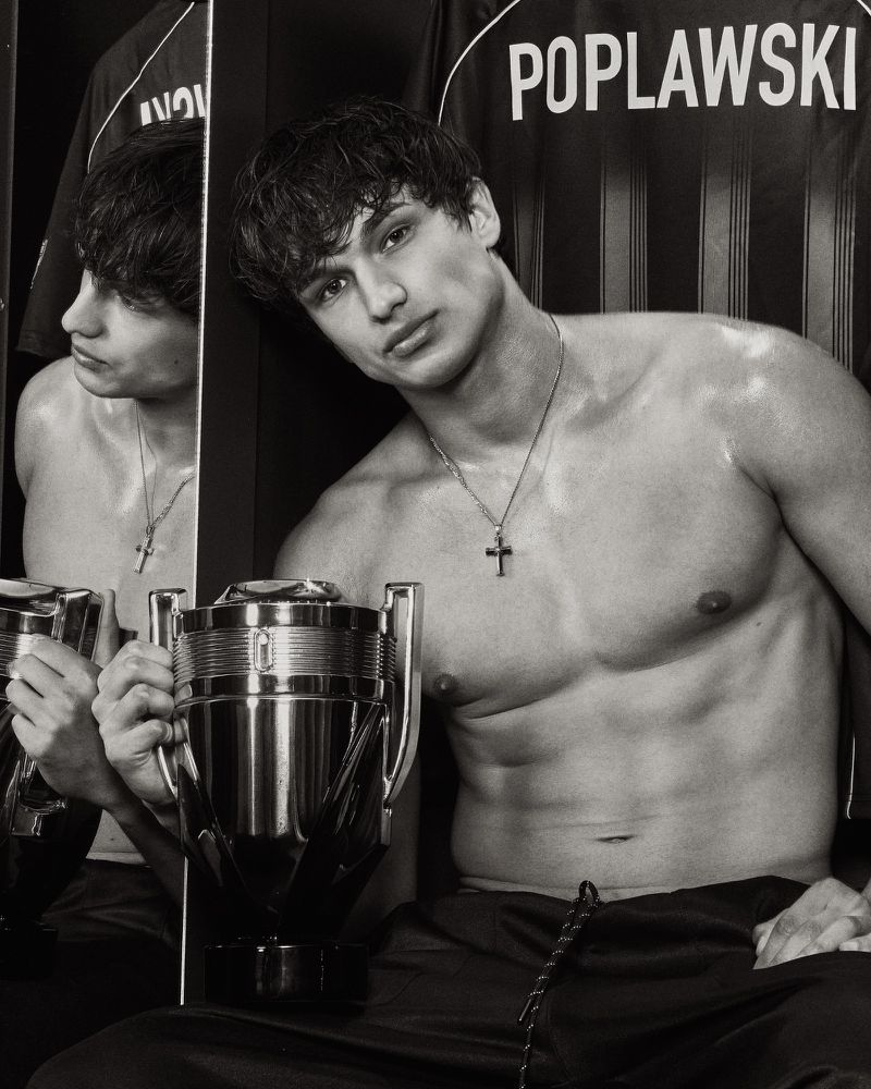 Monochrome portrait of model Giuliano Poplawski holding a trophy-shaped Rabanne Invictus Elixir bottle in a locker room setting.