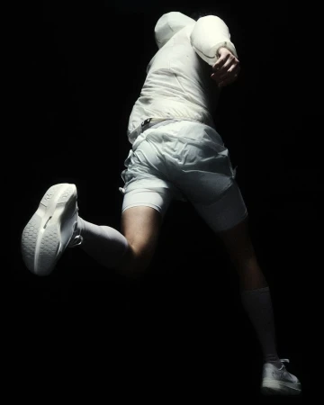Runner mid-stride from a low rear angle wearing an all-white running jacket, shorts, and white sneakers against a black background.