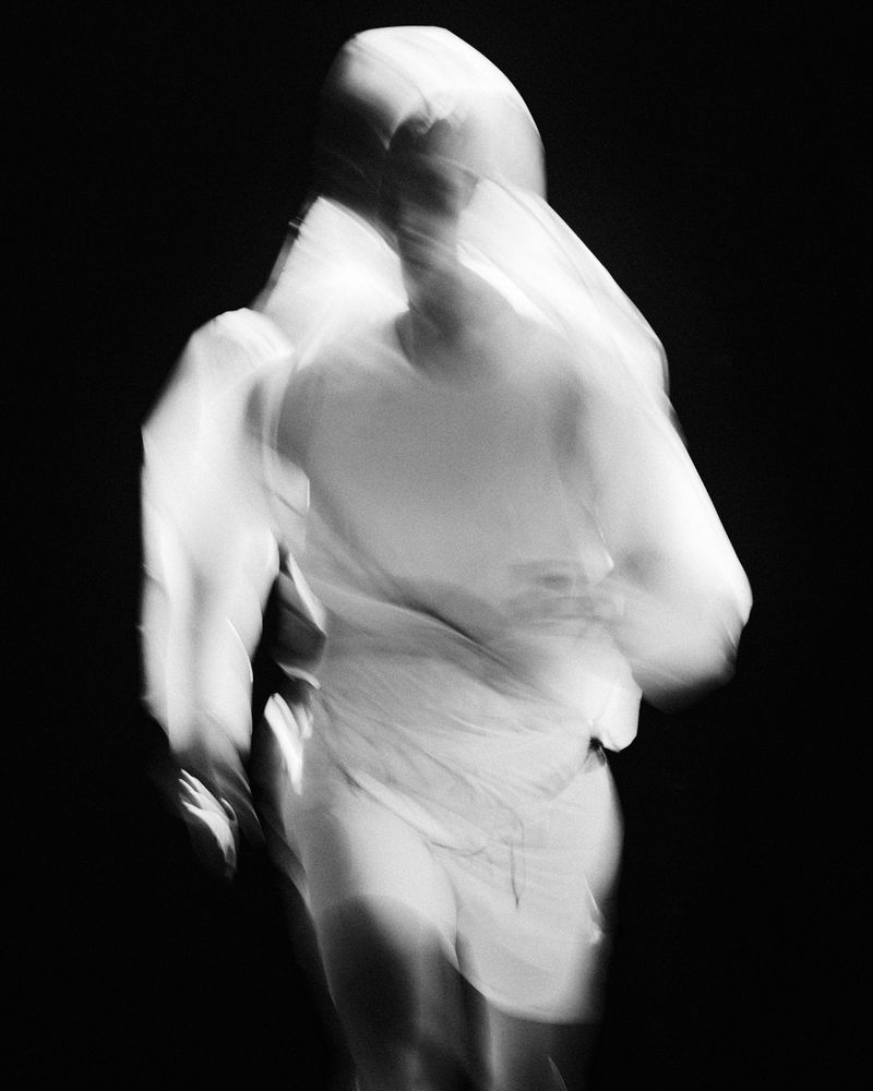 Black and white motion-blurred image of a runner wearing white athletic apparel against a dark background.