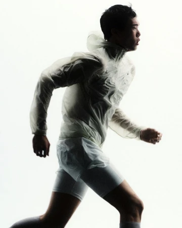 Runner in profile wearing a translucent hooded running jacket and white shorts against a bright white background.