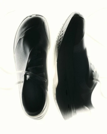 Overhead studio view of a pair of black On Running sneakers displayed against a glowing backlit white background.