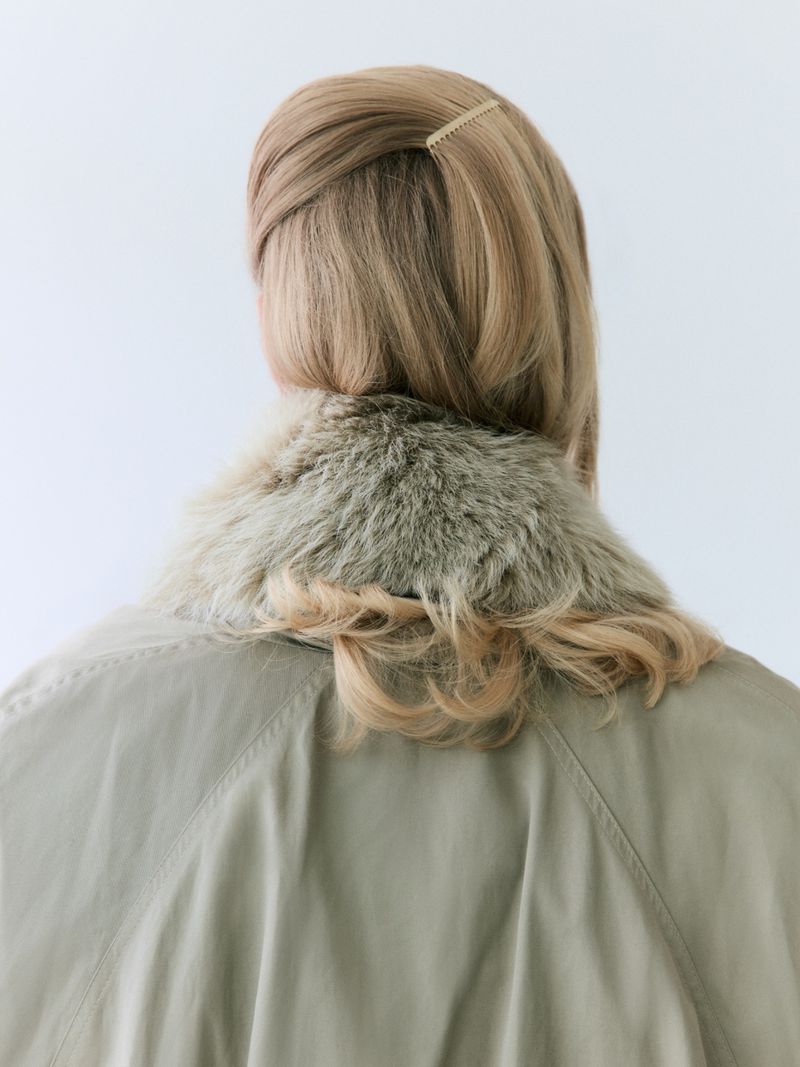 Model Astrid Østergaard viewed from behind wearing a green jacket with a faux fur collar and blonde hair pinned with a comb.