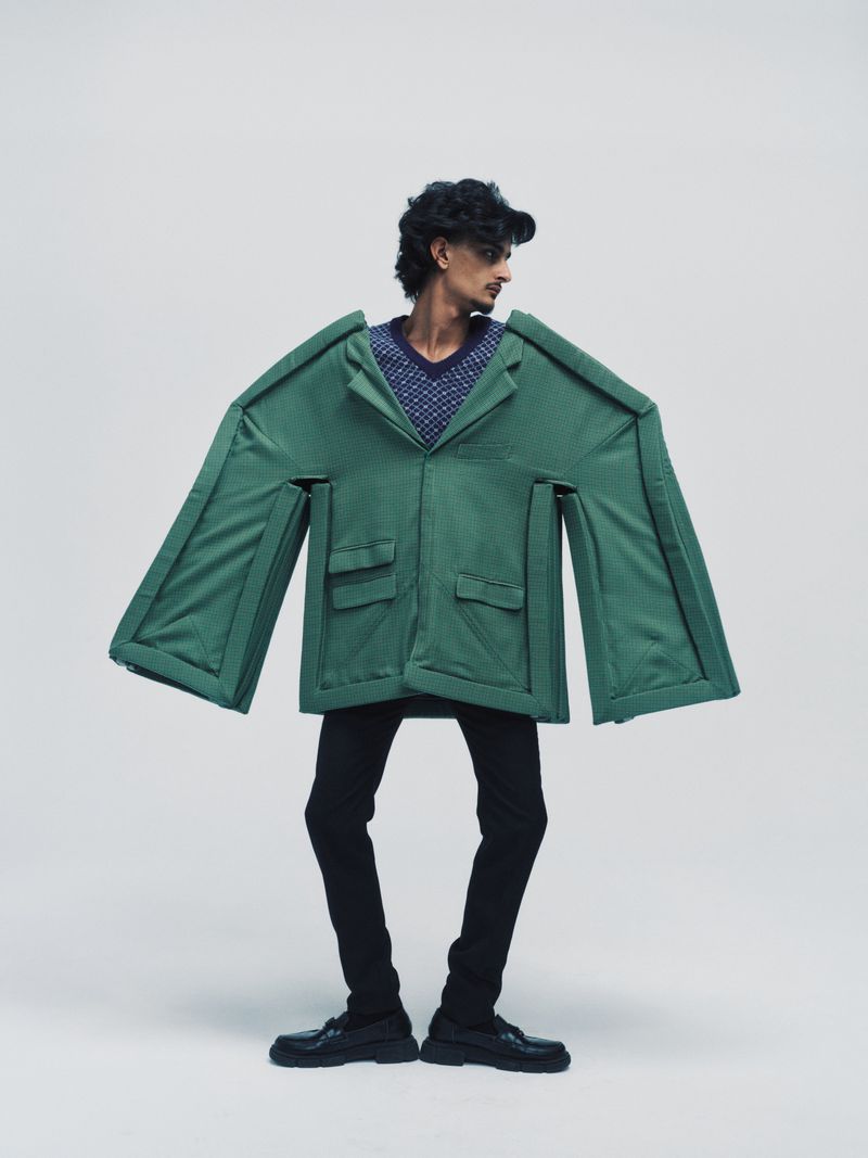 Boyd Gates in an oversized sculptural green geometric jacket with black trousers against a seamless studio background.