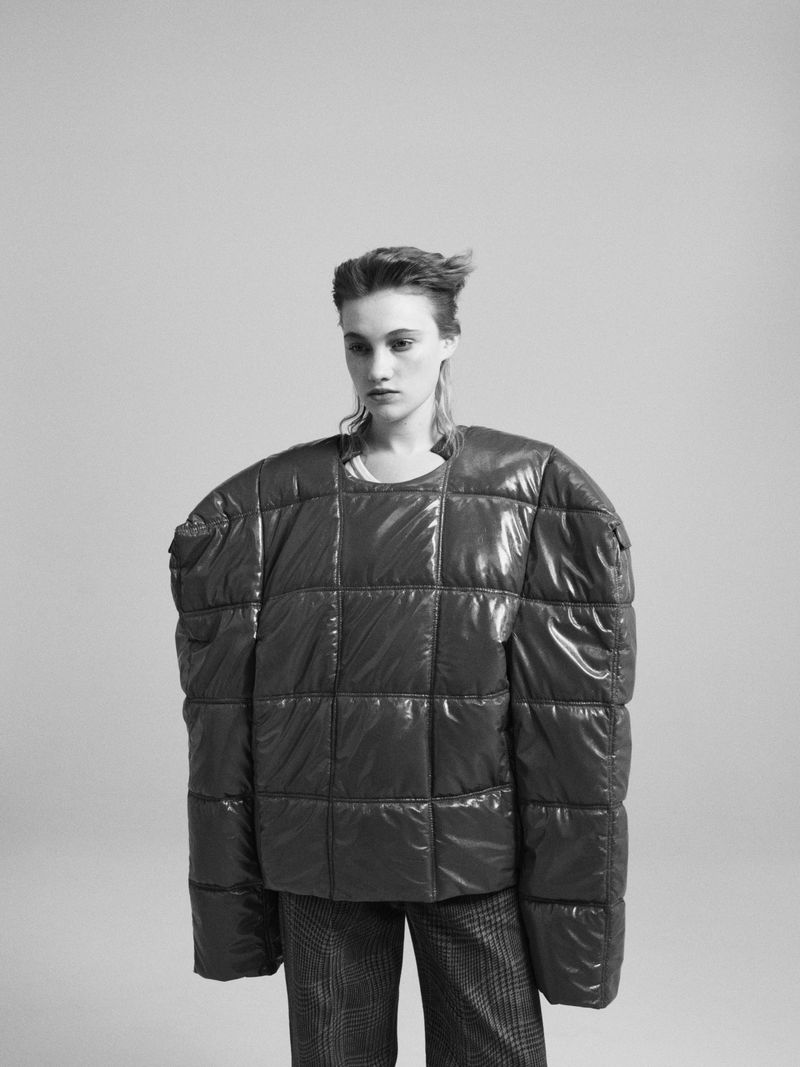 Model Boyd Gates wearing an oversized quilted top with exaggerated shoulders and plaid trousers against a studio backdrop.