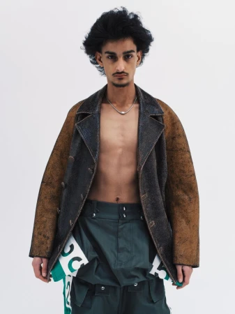 Boyd Gates wearing an open distressed leather jacket and dark green utility trousers against a plain white studio background.