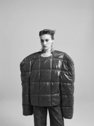 Model Boyd Gates wearing an oversized quilted top with exaggerated shoulders and plaid trousers against a studio backdrop.