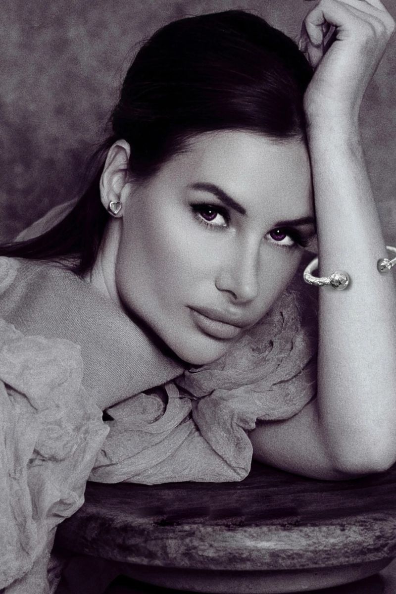 Black and white portrait of a woman resting her head on her hand, wearing a silver cuff bracelet and heart earring.