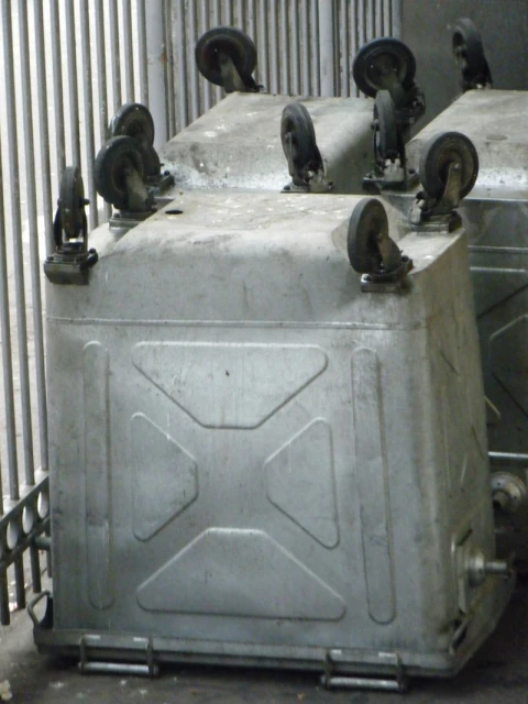 Several metal industrial containers with wheels are positioned indoors, showcasing their design and utilitarian features.