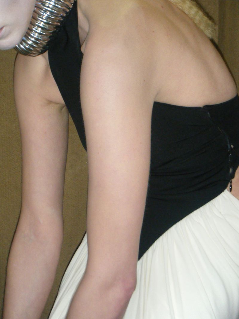 Elegant studio shot of a woman wearing a black top and white skirt, accessorized with a metallic neckpiece, against a neutral backdrop.