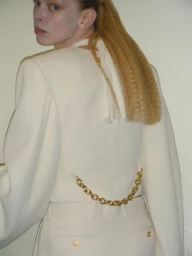 Model seen from behind wearing an off-white structured blazer with a gold chain back detail and matching tailored trousers.