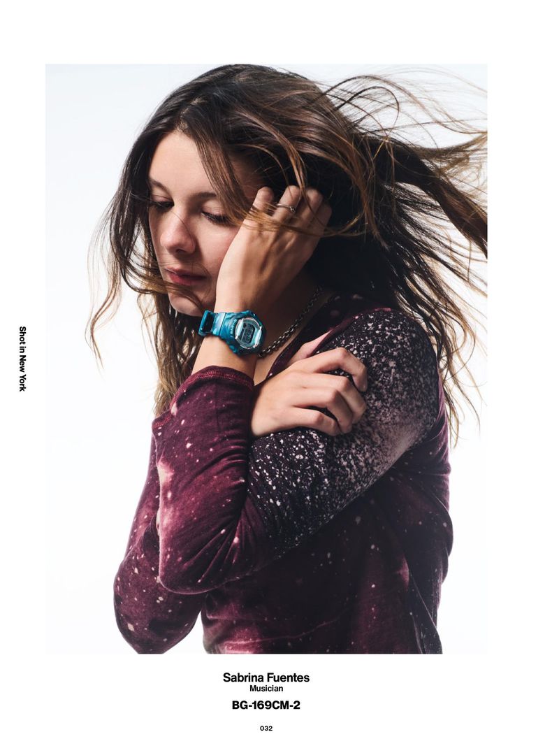 Sabrina Fuentes wearing a teal digital watch and patterned burgundy long-sleeve shirt against a white background.