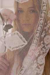 Blonde woman holding a pink rose seen through a sheer embroidered white lace veil.