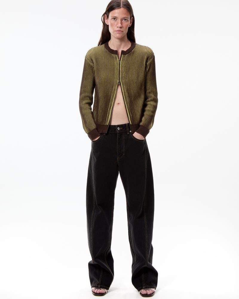 Model Elle Dawson standing in a yellow-green ribbed zip cardigan and wide-leg dark denim jeans against a white background.