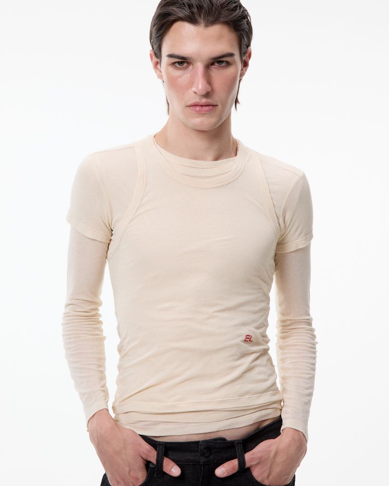 Model Elle Dawson wearing a cream layered long-sleeve t-shirt and black jeans against a white seamless background.