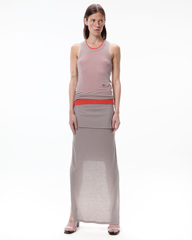Model standing against a plain white background wearing a layered taupe tank top and long skirt over an orange layer