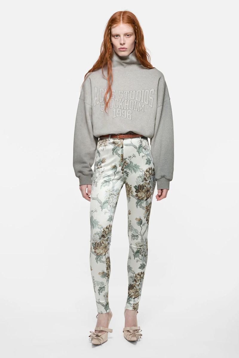 Laura Rudd wears a grey Acne Studios sweatshirt with floral print skinny trousers against a seamless white studio background.