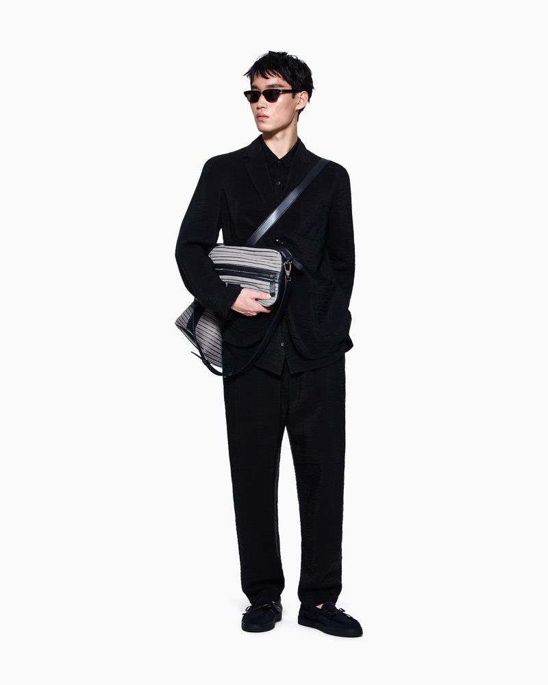 Model Ikko Ohira wearing an all-black suit, sunglasses, and a crossbody bag against a plain white studio background.