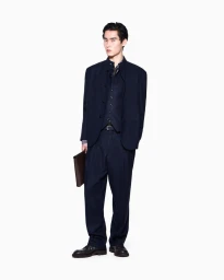 Model Ikko Ohira posing in a navy stand-collar suit, waistcoat, and matching trousers while holding a brown leather portfolio.