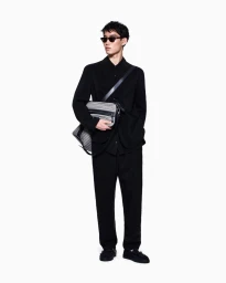 Model Ikko Ohira wearing an all-black suit, sunglasses, and a crossbody bag against a plain white studio background.