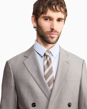 Model wearing a light grey double-breasted suit jacket, light blue collared shirt, and striped tie against a white background.