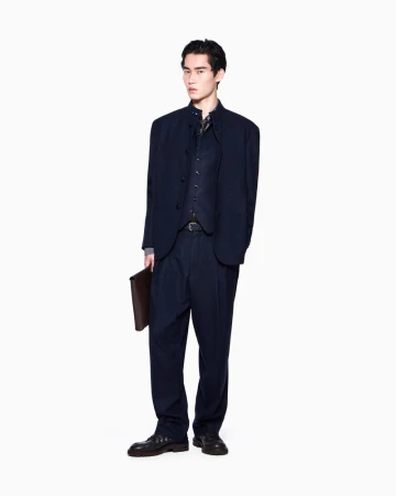 Model Ikko Ohira wears a dark navy suit and holds a brown leather portfolio against a plain white studio background.