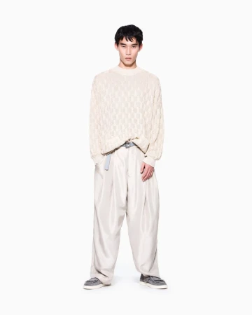 Model standing against a white seamless background wearing an off-white textured knit sweater and loose wide-leg trousers.