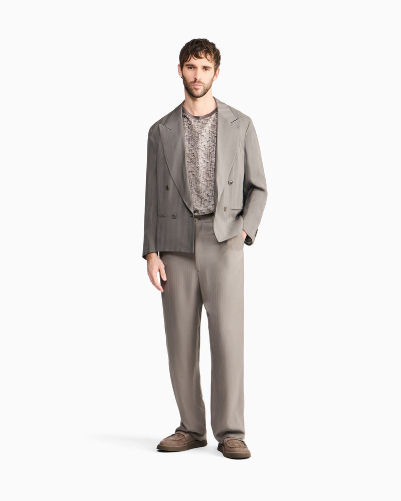 Model Benjamin Demarquilly in a grey tailored jacket and relaxed trousers on a white studio background for Giorgio Armani.